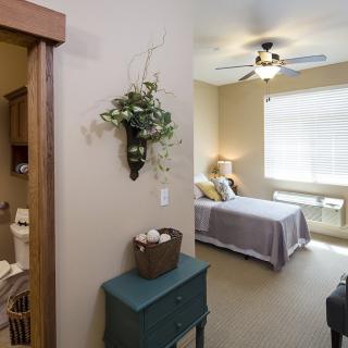 A cozy bedroom with a bed, ceiling fan, and natural light streaming through the window.