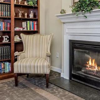 A cozy living room corner with an armchair by the fireplace and a bookshelf.