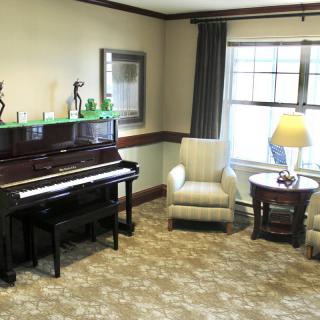 A cozy living room with a piano, armchair, and a lamp by the window.