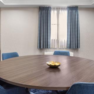A meeting room with a round table and blue chairs, featuring a window with curtains.