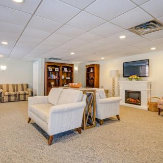 A cozy living room with beige sofas, armchairs, a fireplace, and a TV, complemented by bookshelves and warm lighting.