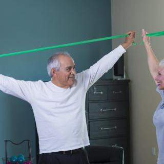 An elderly couple exercises with a resistance band at home.