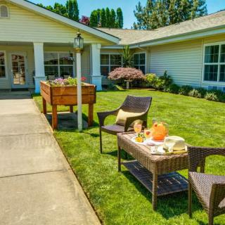 A cozy outdoor patio setup with a table and chairs on a lawn in front of a house.