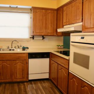 A cozy kitchen with wooden cabinets, an oven, a dishwasher, and a window.