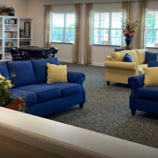 A cozy living room featuring a blue sofa, yellow armchair, and large windows with curtains.