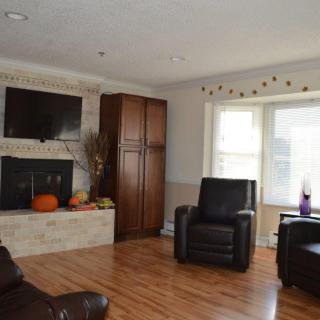 A cozy living room with a fireplace, television, and comfortable armchairs, featuring hardwood floors and bright windows.