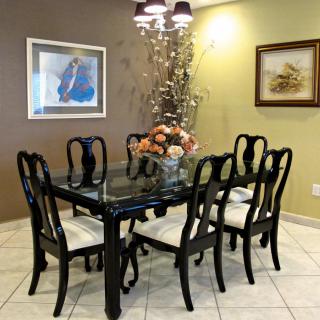 A well-furnished dining room with a black glass-top table surrounded by chairs, featuring elegant decor and artwork on the walls.