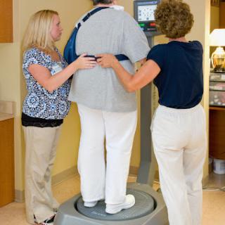Two healthcare professionals assist a patient on a balance or body composition scale.