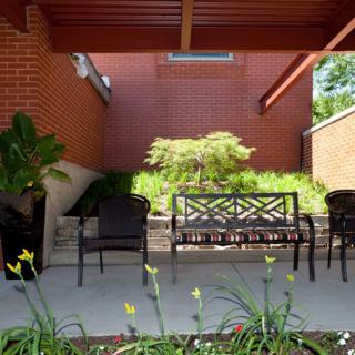 Outdoor patio area with a bench and chairs surrounded by plants.