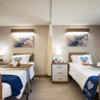 A modern and well-designed hospital room featuring two beds, ambient lighting, and decorative artwork.