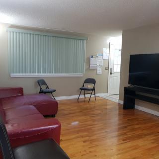 A living room with a red sofa, folding chairs, and a large TV on a wooden floor.