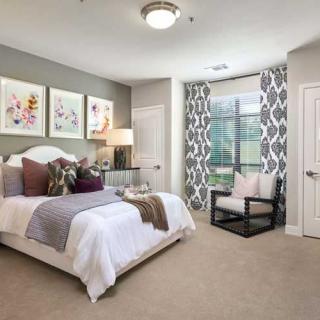 A modern bedroom with stylish decor, featuring a comfortable bed, decorative artwork, and patterned curtains.