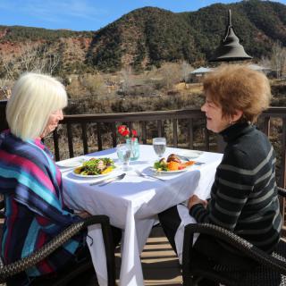 Two women enjoying a meal on a patio with a scenic mountain view.