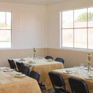 A neatly arranged dining area with tables covered in beige tablecloths, set with dishes and surrounded by chairs.