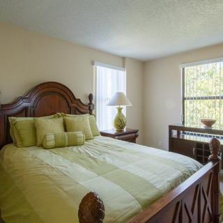 A cozy bedroom with a wooden bedframe, green bedding, and natural light from two windows.