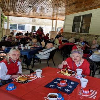 Residents enjoying a festive meal outdoors, adorned in red with patriotic decorations.