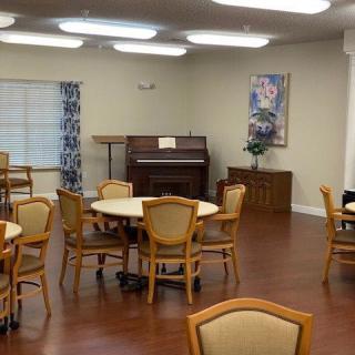 A community dining area with several round tables, chairs, and a piano in the corner.