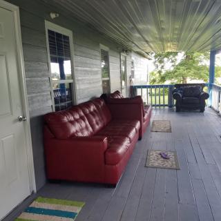 A cozy porch with a red sofa and rugs on a wooden floor.