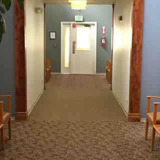 A quiet hallway with chairs lining the walls and a carpeted floor, leading to an exit door.