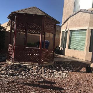 A sunny backyard featuring a wooden gazebo and desert landscaping.