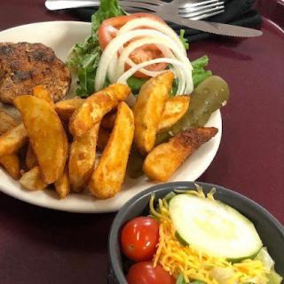 A delicious plate featuring seasoned fries, a fresh salad with tomatoes and onions, and a side of pickles.