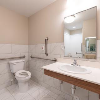 A modern bathroom featuring a toilet, sink, and handrails for accessibility.