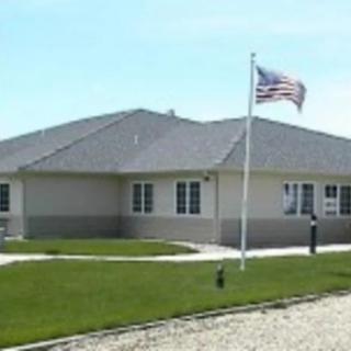 A single-story building with an American flag displayed on a pole in the front yard.