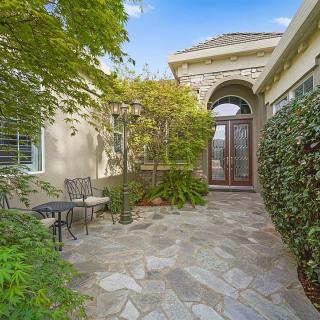 A charming house entrance with a stone path and outdoor seating area surrounded by lush greenery.