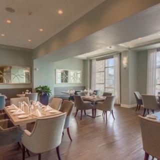 An elegant restaurant interior with well-arranged dining tables and chairs, accentuated by natural light from large windows.