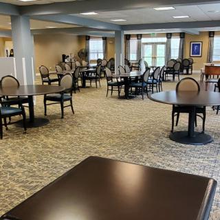 A spacious dining area with neatly arranged tables and chairs, featuring large windows and a carpeted floor.