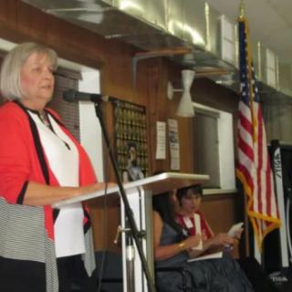 A woman speaks at a podium with an American flag in the background.