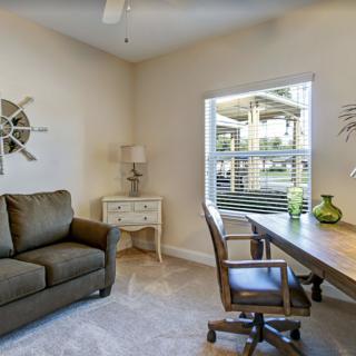 A cozy home office with a desk, chair, and sofa, featuring decorative elements and a window view.