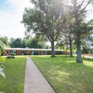 A sunny day view of a building surrounded by trees and a well-maintained lawn, with a pathway leading towards it.