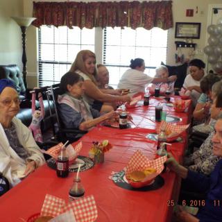 A group of people gathered around a dining table for a celebration, with food and drinks on the red tablecloth.