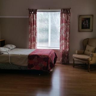 A cozy bedroom with a bed next to a window, adorned with red curtains and an armchair in the corner.
