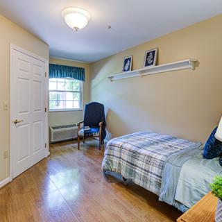 A cozy bedroom with a single bed, wooden flooring, and a window letting in natural light.