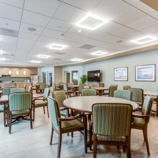 A spacious dining area with multiple tables and chairs, featuring modern lighting and a television on the wall.