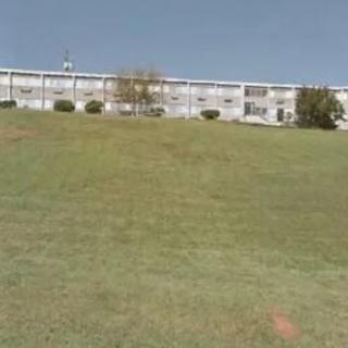 A building at the top of a grassy hill under a clear sky.