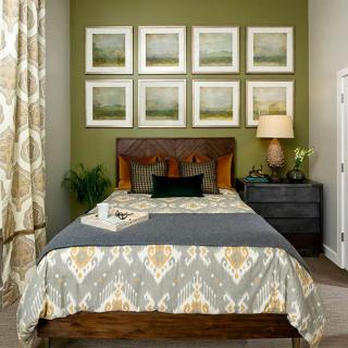A cozy bedroom with a stylish interior, featuring a neatly made bed, framed artwork on the wall, and a side table with a lamp and plant.