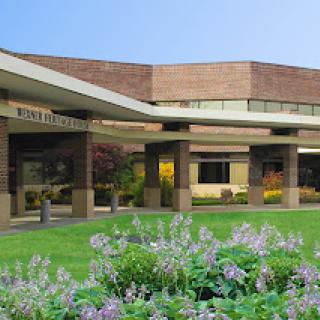 A view of a medical facility featuring modern architecture, surrounded by lush greenery and colorful flowers.