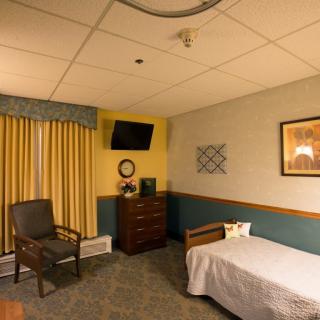 A cozy bedroom with a single bed, a chair, a dresser, and a wall-mounted television.