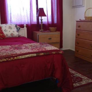 A cozy bedroom with red-themed decor, featuring a bed, dresser, and lamp.