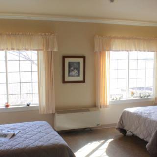 A bright bedroom with two beds and large windows letting in natural light.