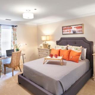 A modern and cozy bedroom featuring a neatly made bed with orange accent pillows and a small desk area beside it.