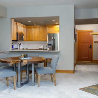 A modern open-plan dining area with a view into the kitchen, featuring wooden furniture and a carpeted floor.