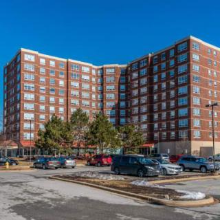A large residential apartment building with a parking lot in the foreground under a clear blue sky.