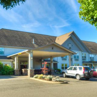 A hotel with a covered entrance and parked cars in the parking lot.