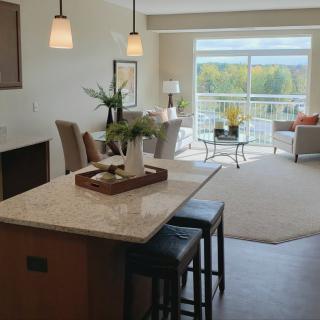 A modern open-concept living and dining area featuring a kitchen island with stools and large windows allowing natural light to fill the space.