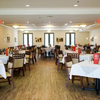 The interior of a restaurant with neatly arranged tables and chairs, adorned with white tablecloths.