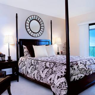 A beautifully decorated bedroom featuring a four-poster bed with patterned bedding, complemented by bedside lamps and a decorative wall mirror.